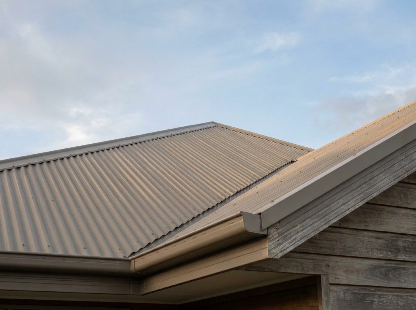 The edge of a corrugated steel roof and its gutter against an open sky