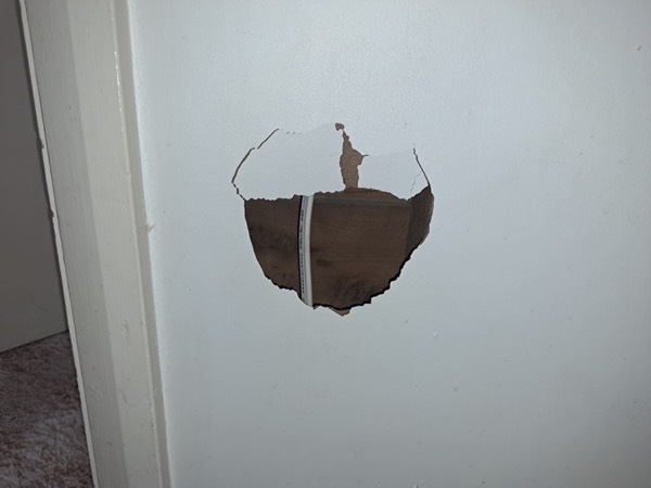 A hole broken through a plasterboard wall beside a door frame