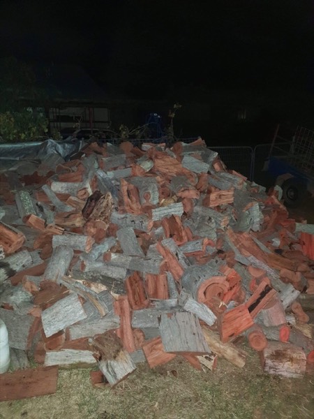 A large pile of split firewood stacked on a yard at night