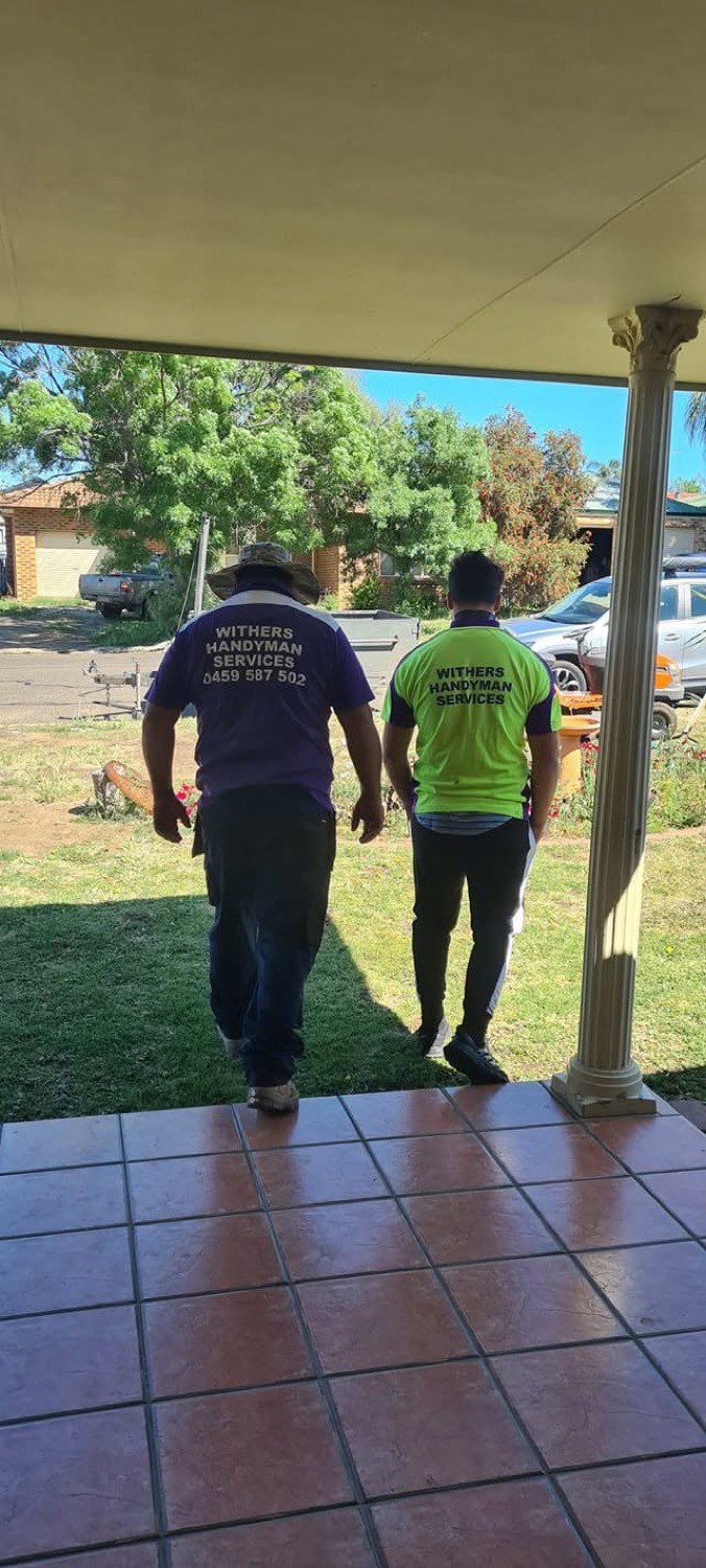 Two people in Withers Handyman Services shirts walking across a front lawn towards a house