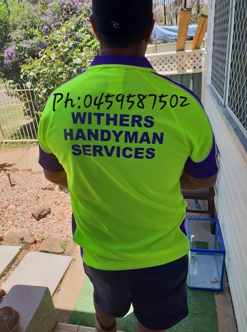 A person in a Withers Handyman Services shirt working at the side of a house