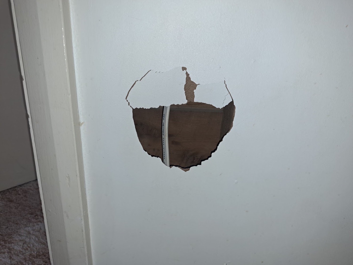 A hole broken through a plasterboard wall beside a door frame