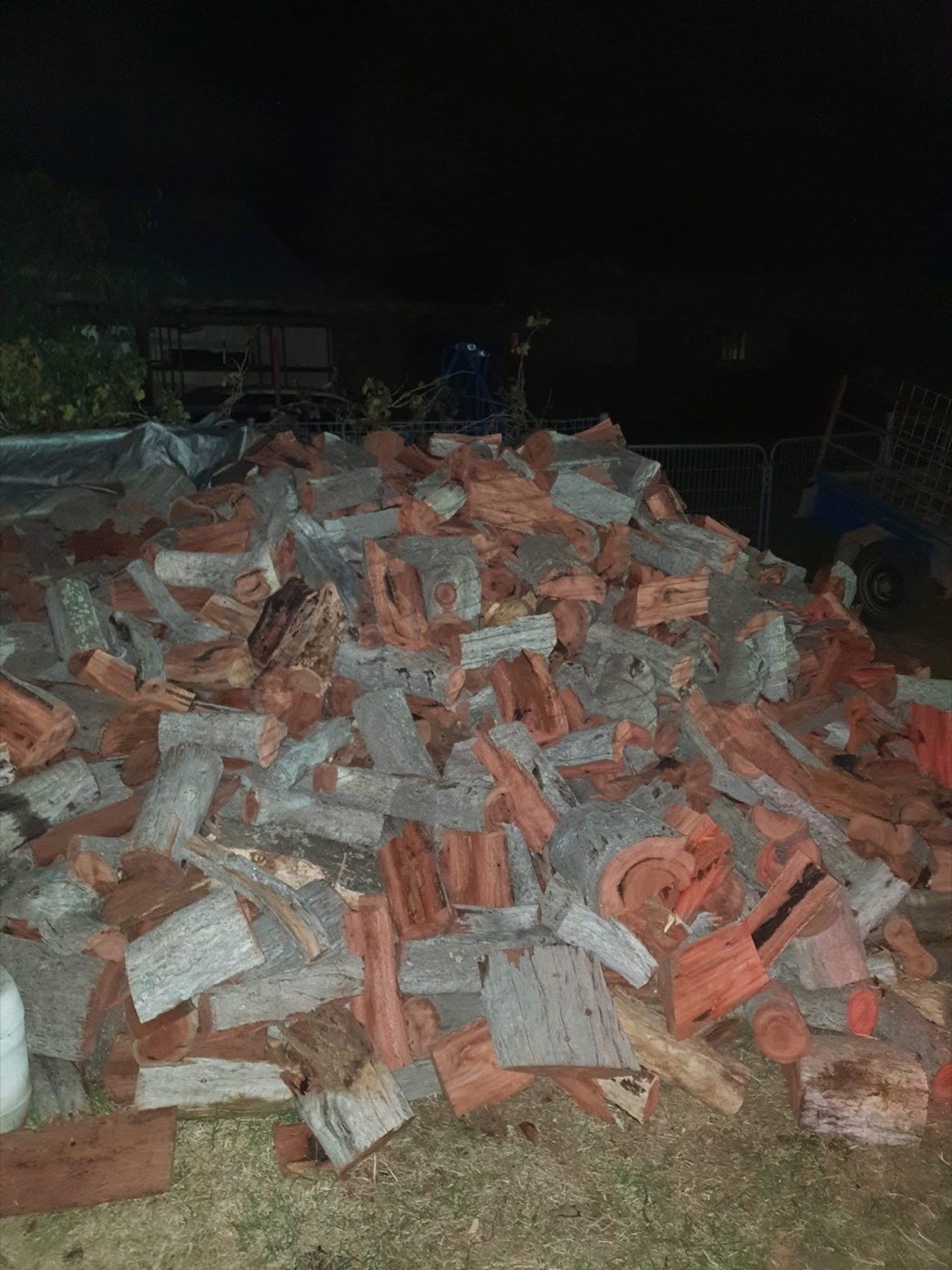 A large pile of split firewood stacked on a yard at night